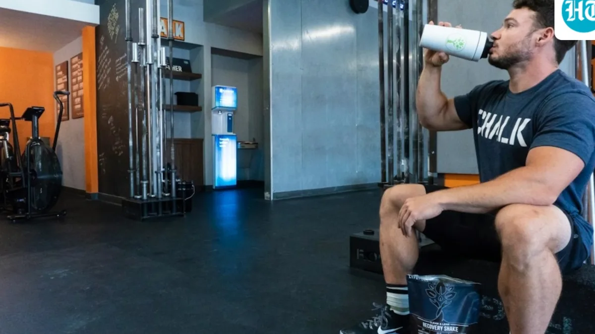 Coach Raj Ganpath in a gym setting, with a background of fitness equipment and a cityscape