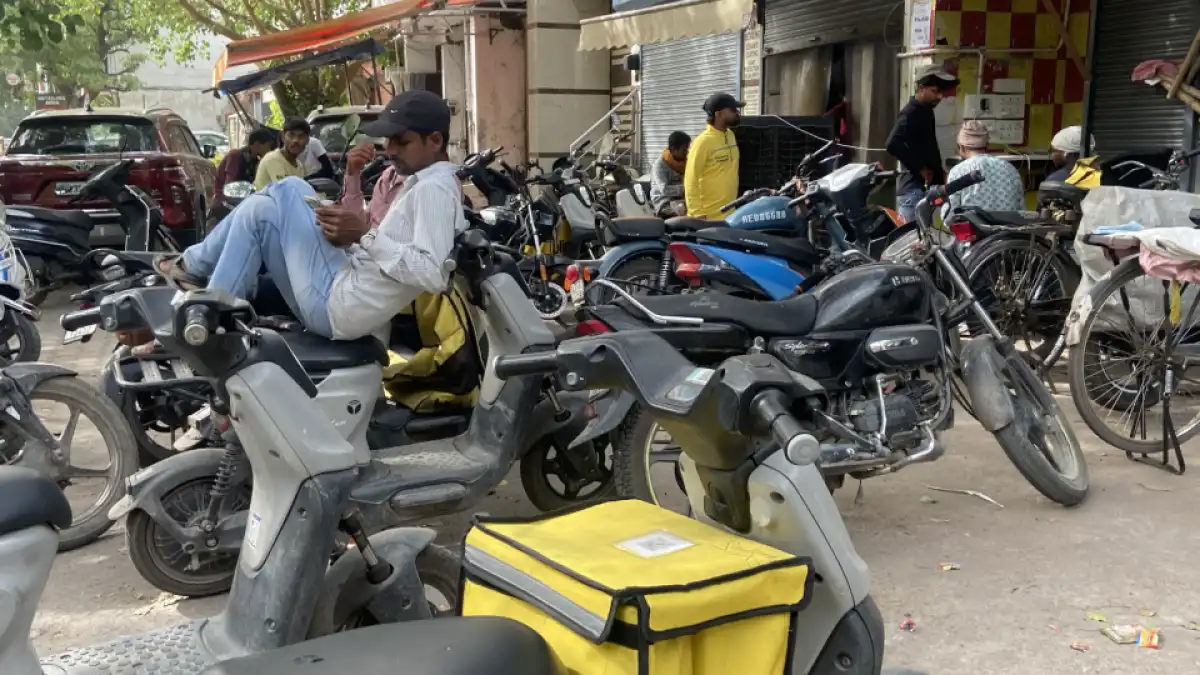 A tired delivery rider standing near a roadside rest area in an Indian city